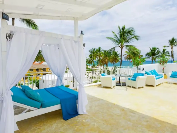 a white canopy with blue pillows and blue blankets on a patio with palm trees
