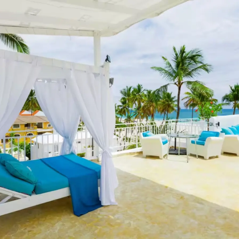 a white canopy with blue pillows and blue blankets on a patio with palm trees